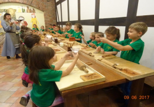 Dzieci siedzą przy dużym stole z akcesoriami potrzebnymi do wyrobu ciasta.